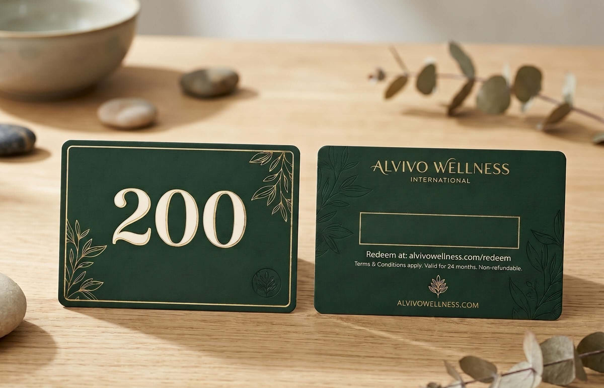 Two dark green gift cards with gold detailing are displayed on a light wood tabletop. The front card shows the number 200 in raised cream lettering, and the back card displays the brand name 'AURA WELLNESS INTERNATIONAL' with redemption details.