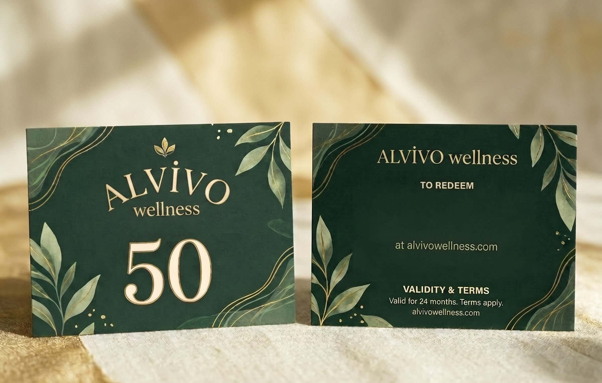Two dark green and gold table cards for 'ALVIVO wellness  Gift Card' displayed side-by-side on a textured beige fabric background. The left card features the number 50 in gold, and the right card displays redemption details.