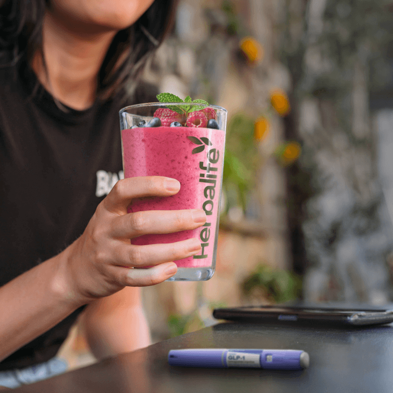 GLP-1 Nutrition Companion Vegan smoothie in a Herbalife glass garnished with berries and mint.